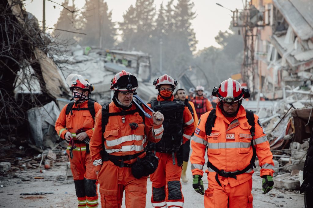 Photographer Faruk Tokluoğlu. Search and rescue team in orange uniforms in a demolished area, assessing damage and carrying out operations.